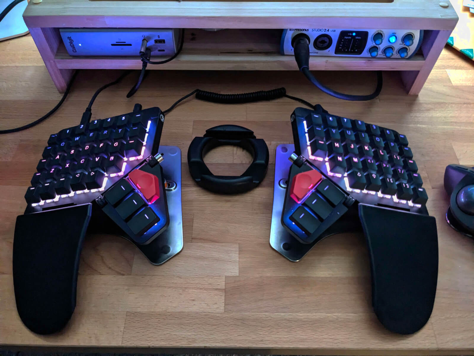 My Moonlander keyboard, illuminated on my wooden desktop in a range of blue, pink, purple and white